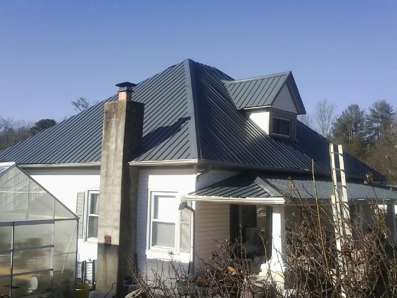 Dark blue standing seam metal roof on a white farmhouse with dormer — Slate & Tile Roof Repair by Roofing Brothers in Pooler
