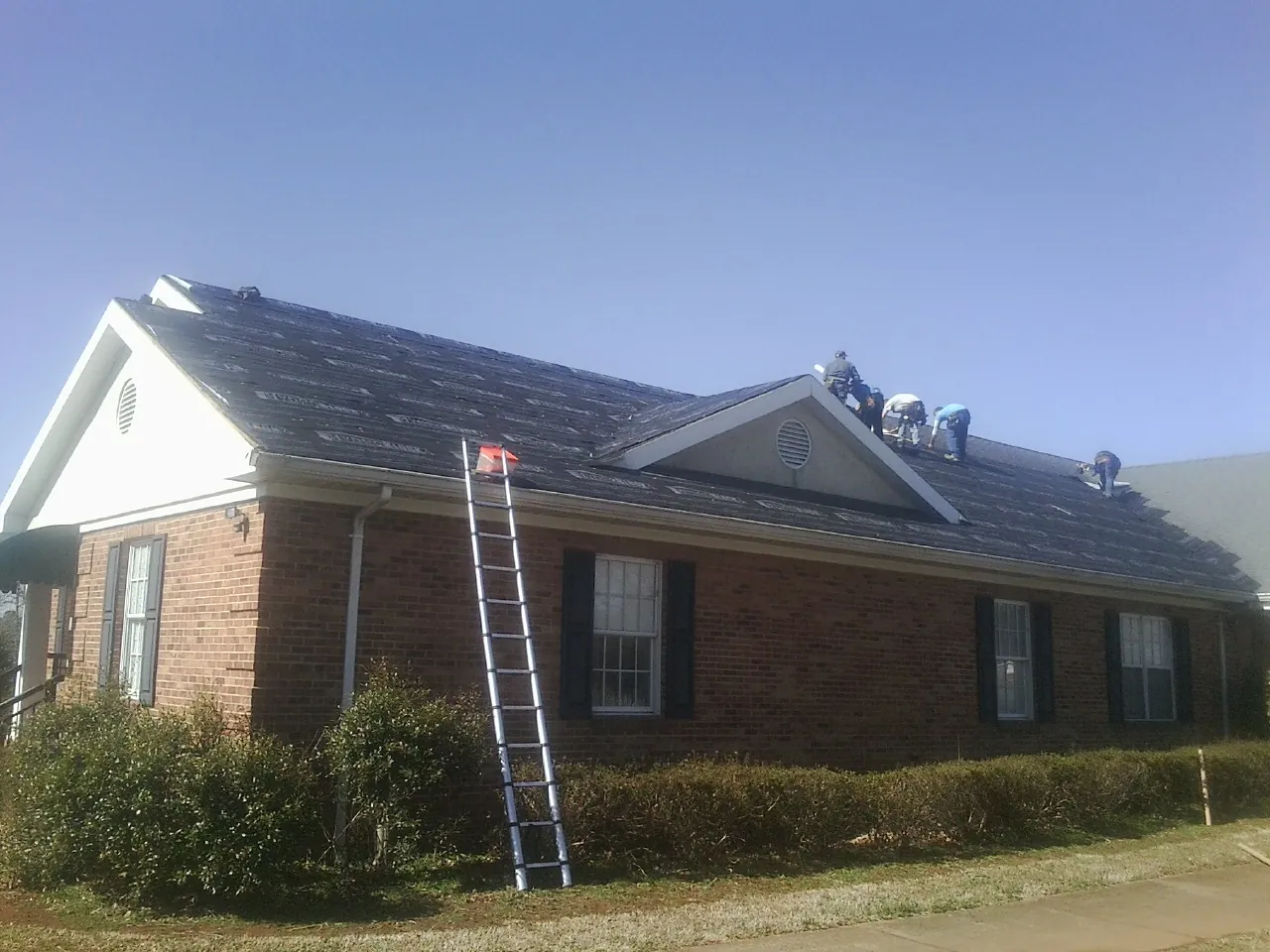 Crew tearing shingles off a brick ranch roof with a ladder set — Emergency Roof Repair work by our crew in Pooler