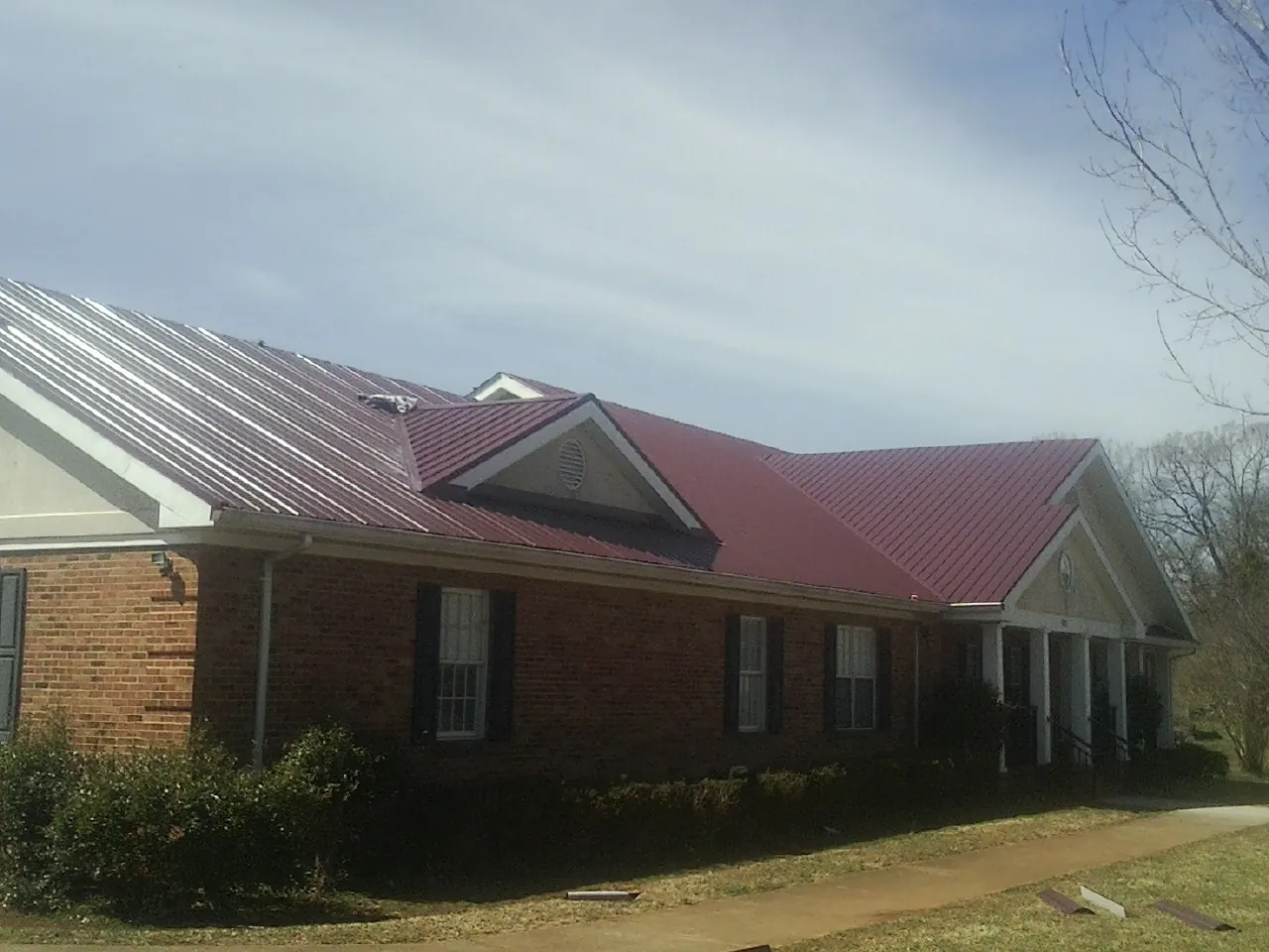 Red metal roof with gabled entries on a long brick building, from a Hail Damage Roof Repair job in Pooler