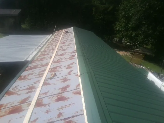 Old rusted panels beside newly installed green metal roofing — Wind Damage Roof Repair by Roofing Brothers in Pooler