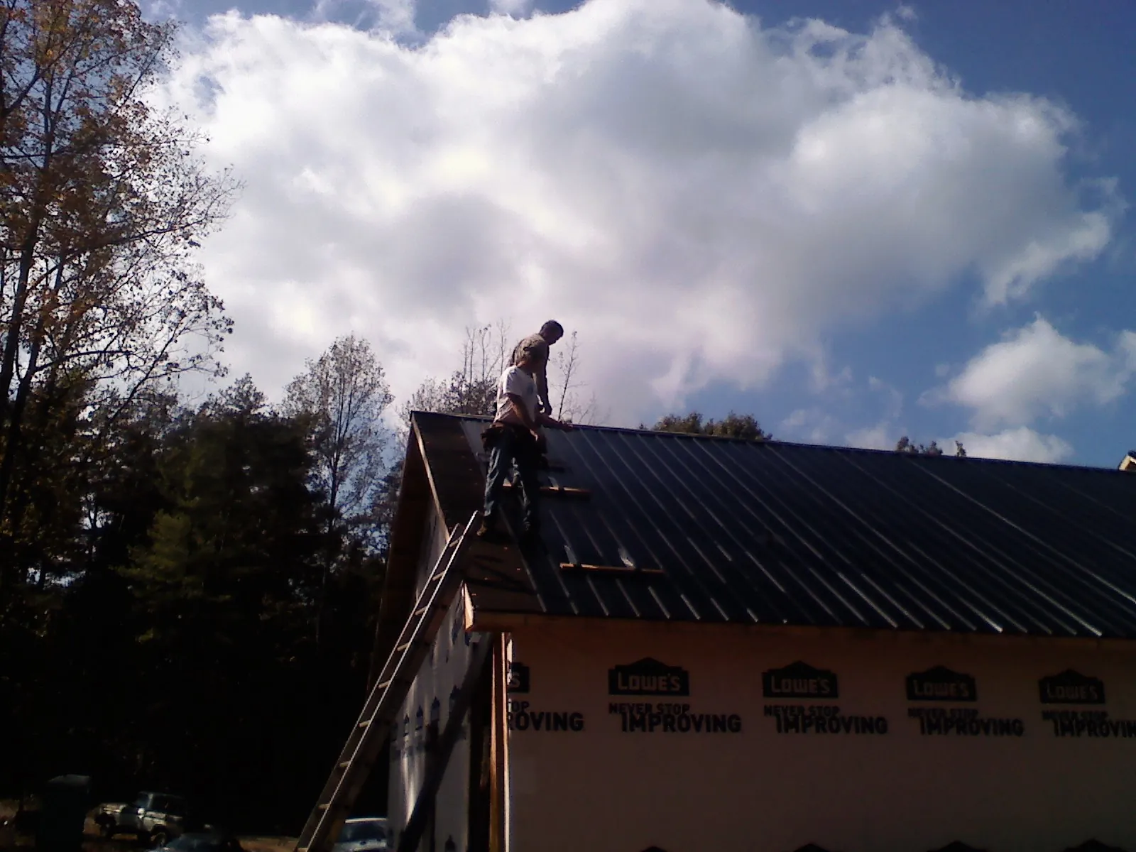 Roofer fastening dark metal panels high against a cloudy sky, from a Roof Inspection job in Pooler
