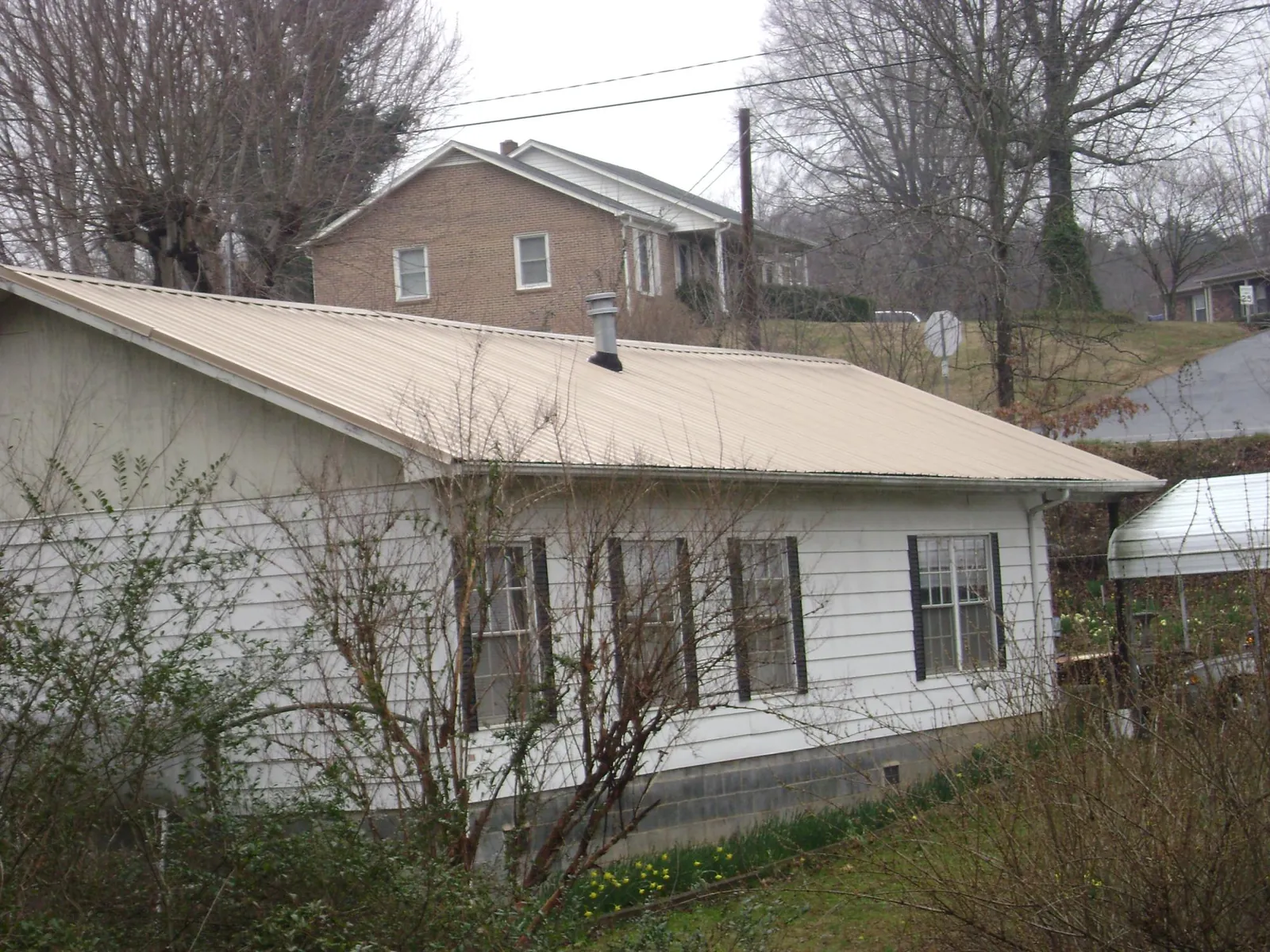 Tan metal roof on a white sided house set into a hillside — Commercial Roofing by Roofing Brothers in Pooler